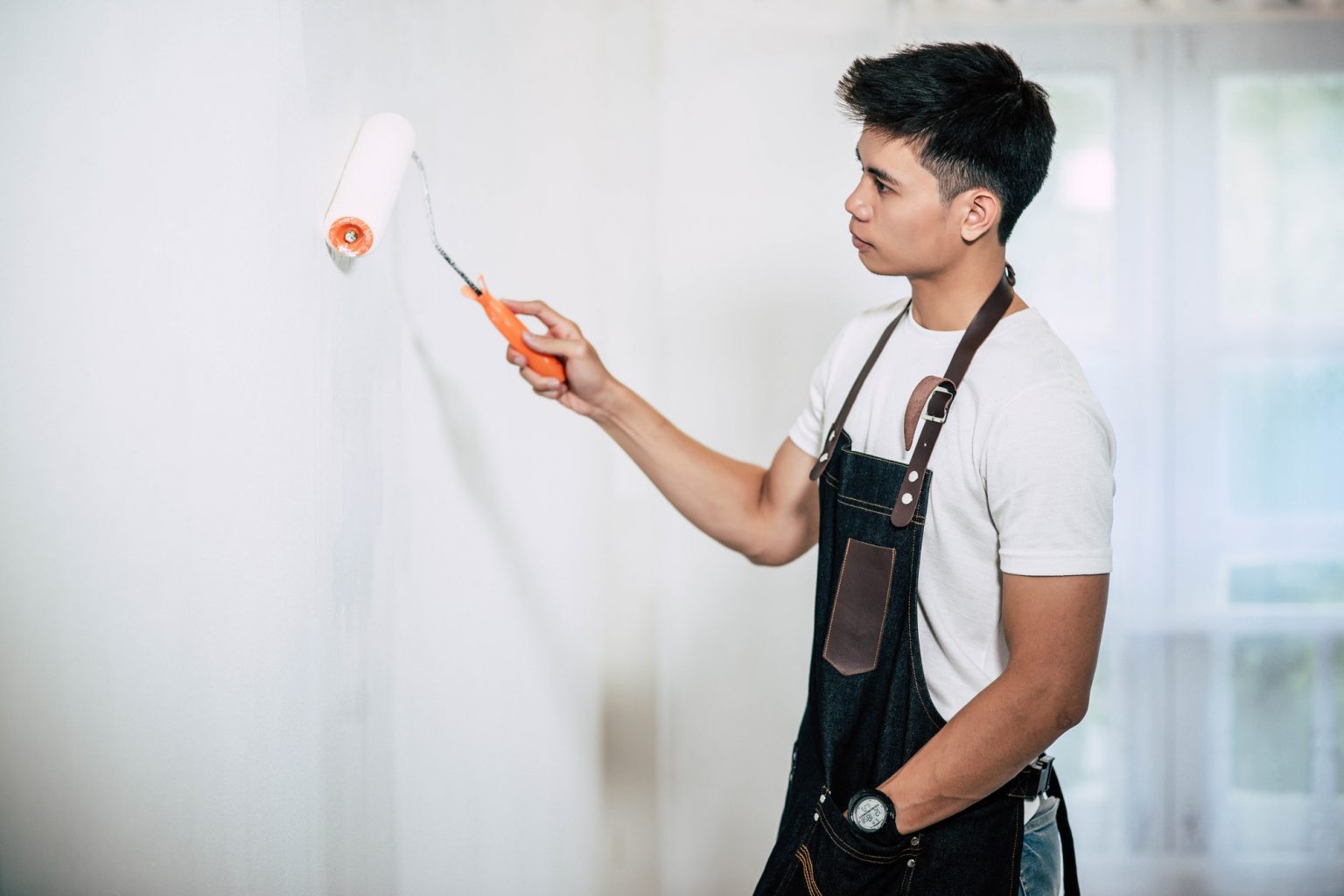 A carpenter holds a paintbrush and paints wood.